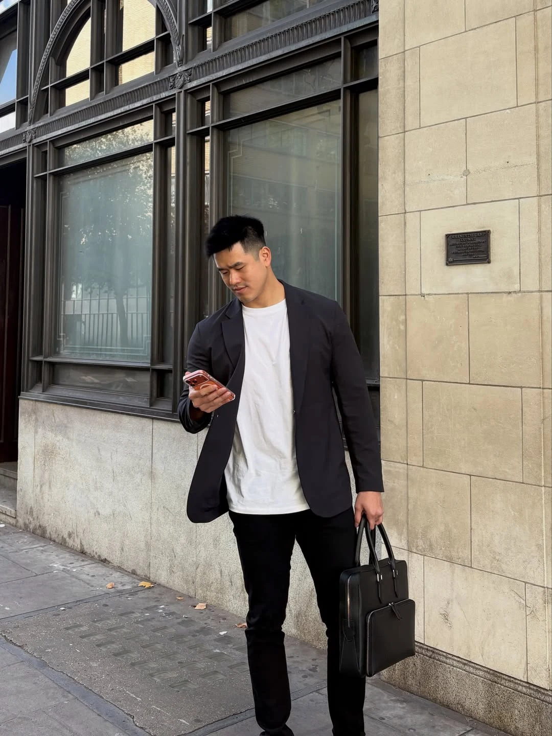 Alex Chee 穿深色西装外套和白色上衣站在街边，查看手机