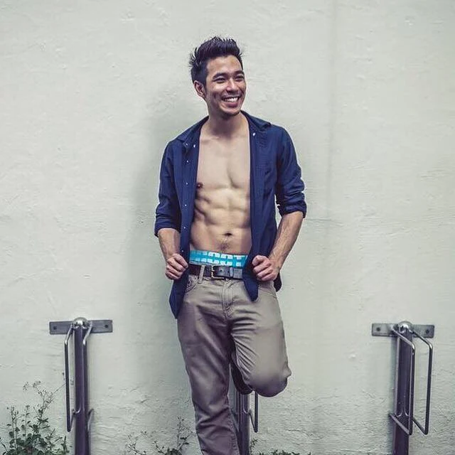 Gabriel Lu 穿敞开的蓝色衬衫与长裤站立，展示胸腹线条