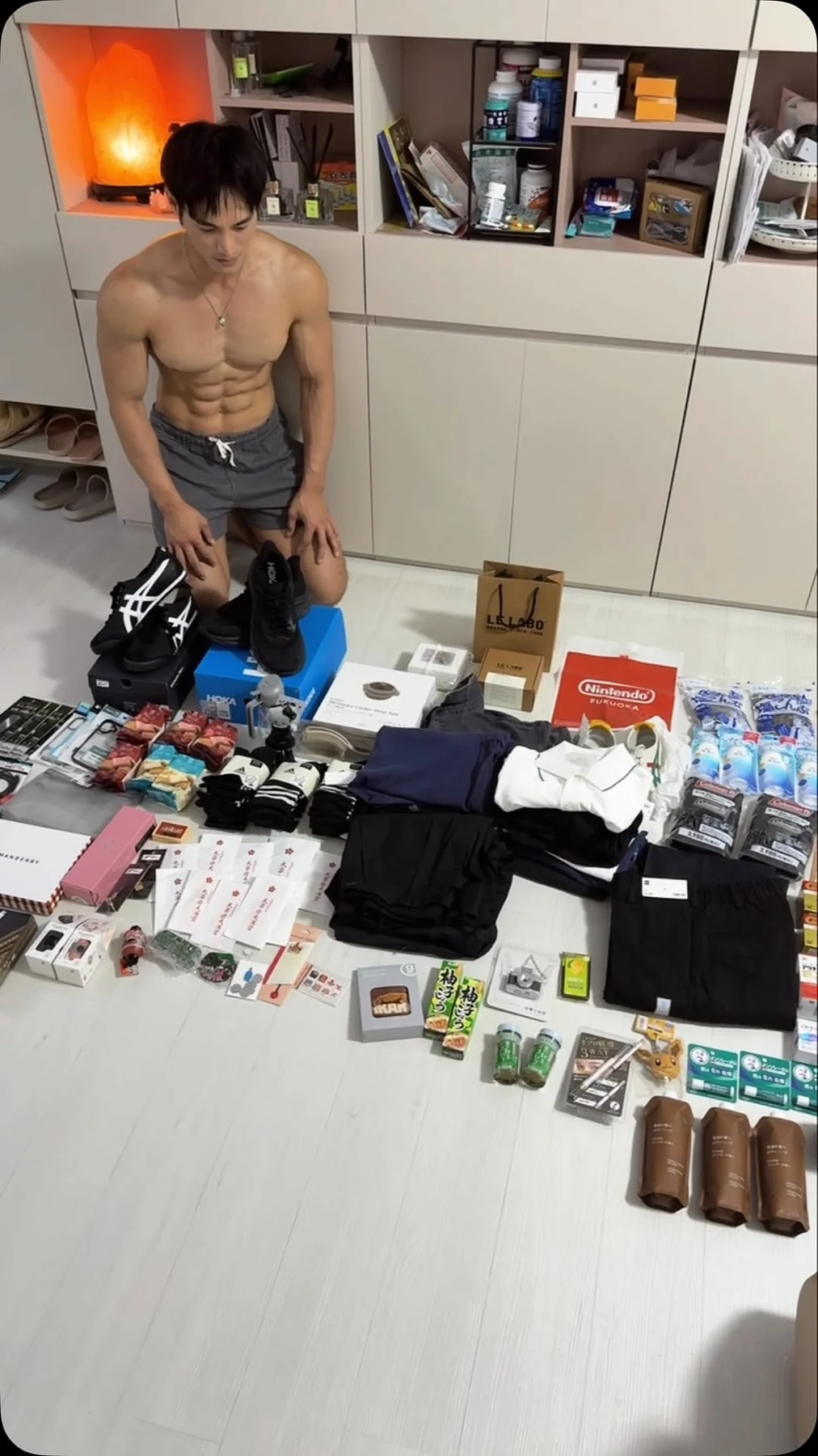 约翰赤膊穿深色短裤，在摆放衣物的房间镜前自拍展示腹肌